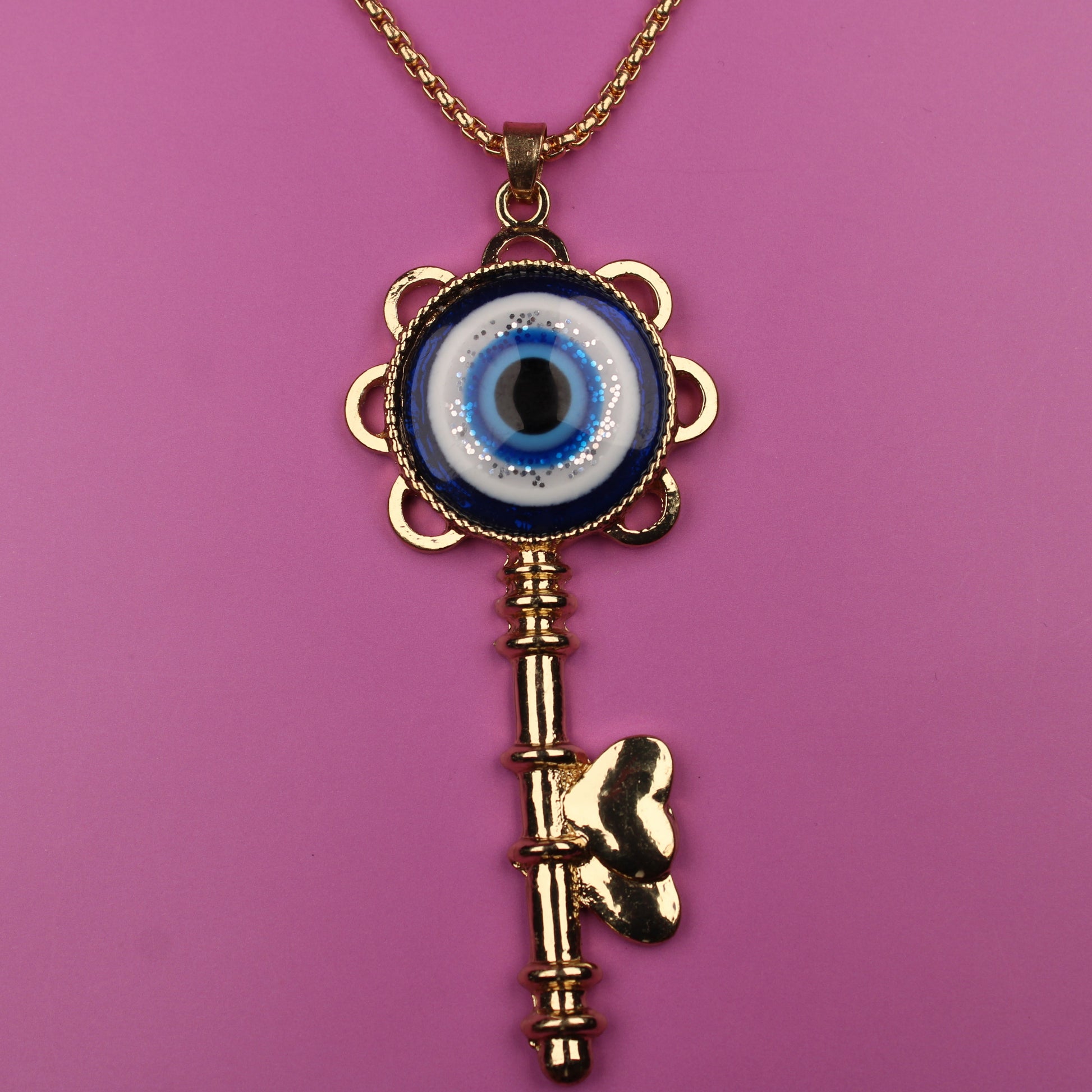 Gold key-shaped necklace with an eye design on a pink background