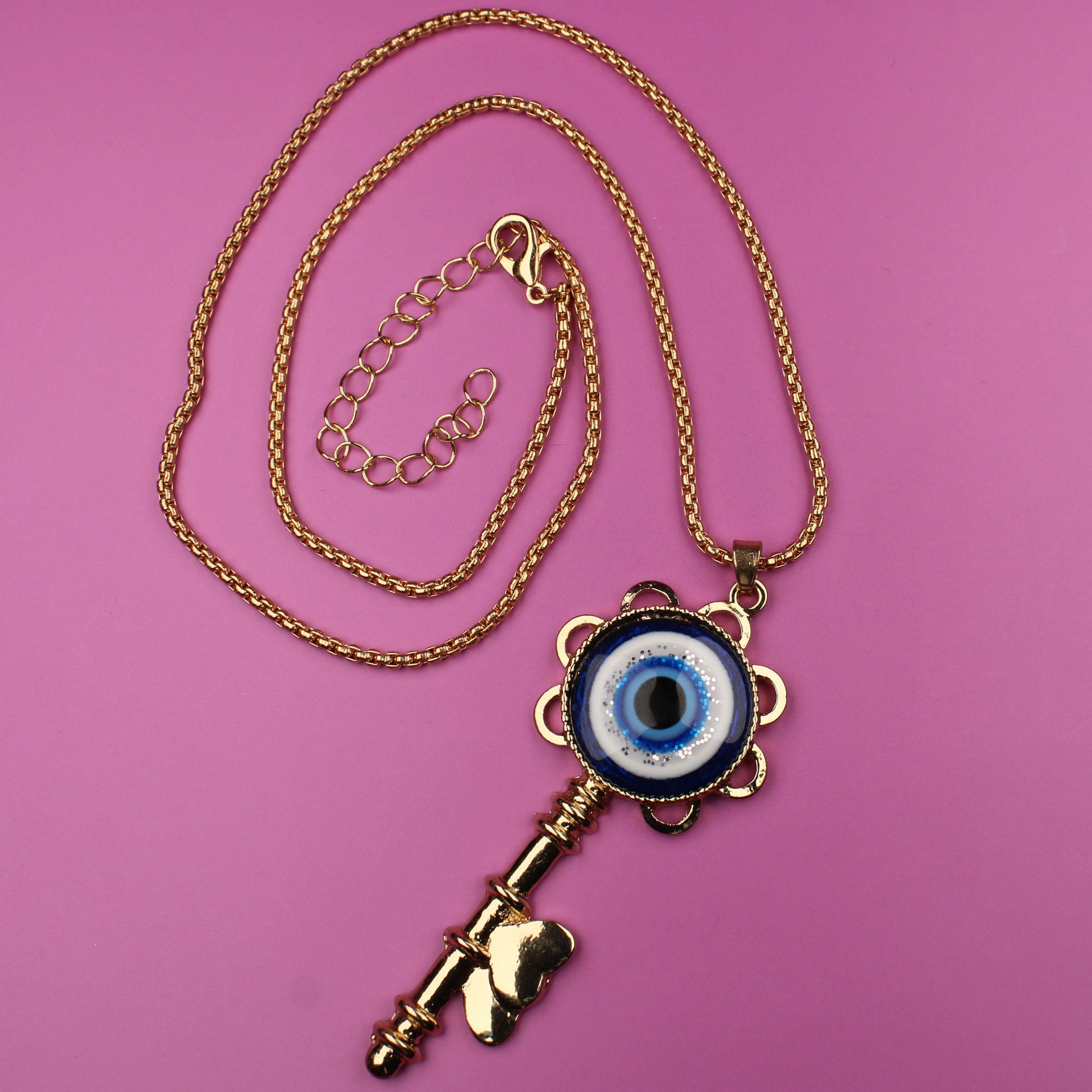Gold key-shaped necklace with an eye pendant on a pink background