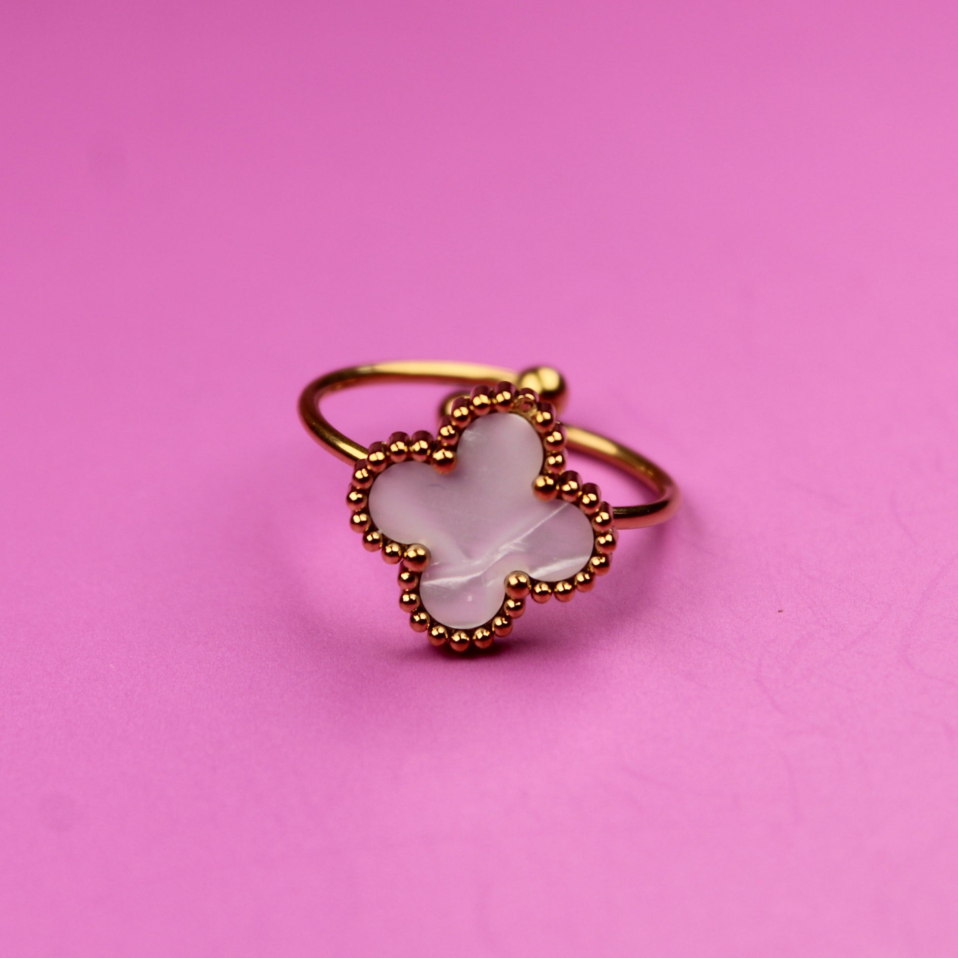 Gold ring with a white stone on a pink background