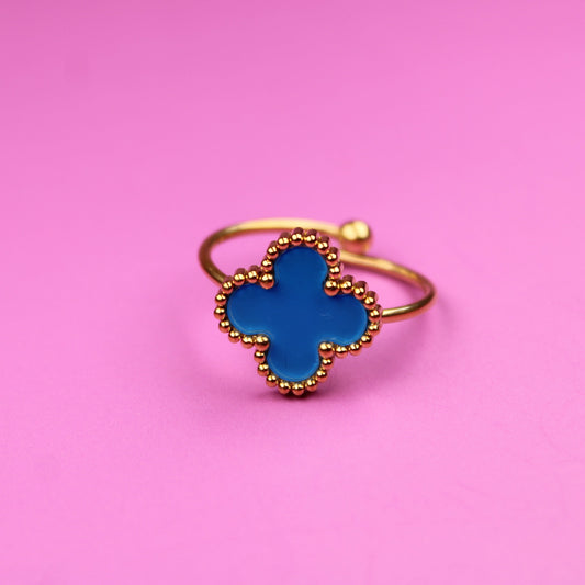 Gold ring with a blue clover-shaped stone on a pink background