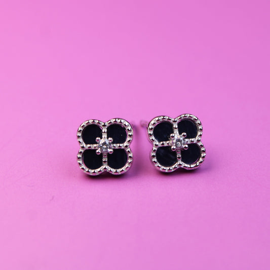 Black clover-shaped earrings on a pink background