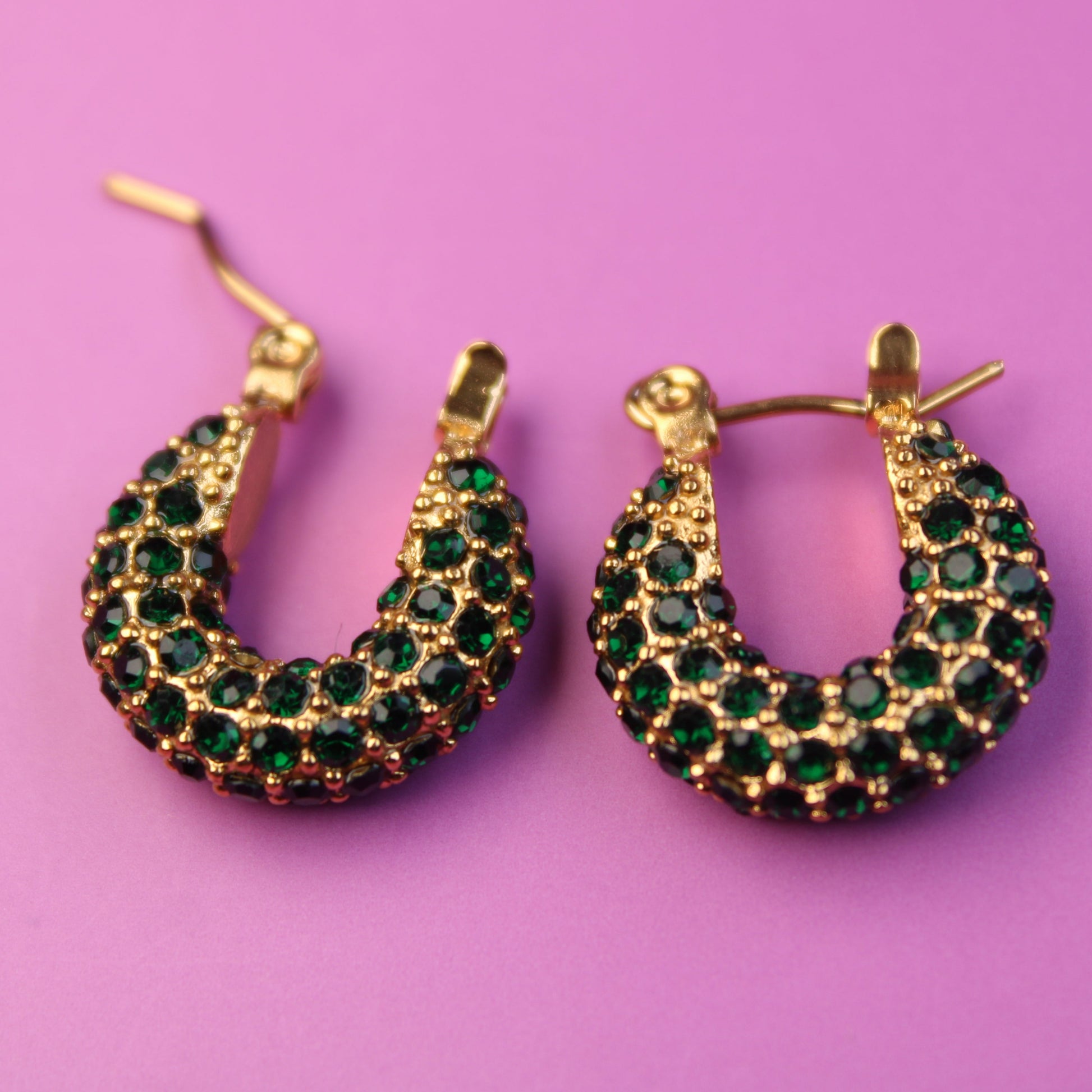 Gold hoop earrings with green gemstones on a pink background
