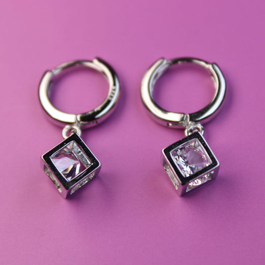 Pair of silver hoop earrings with square gemstones on a pink background