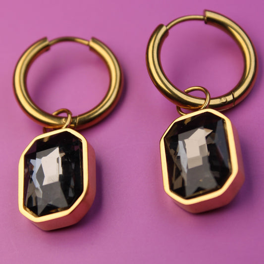 Gold hoop earrings with black gemstones on a purple background