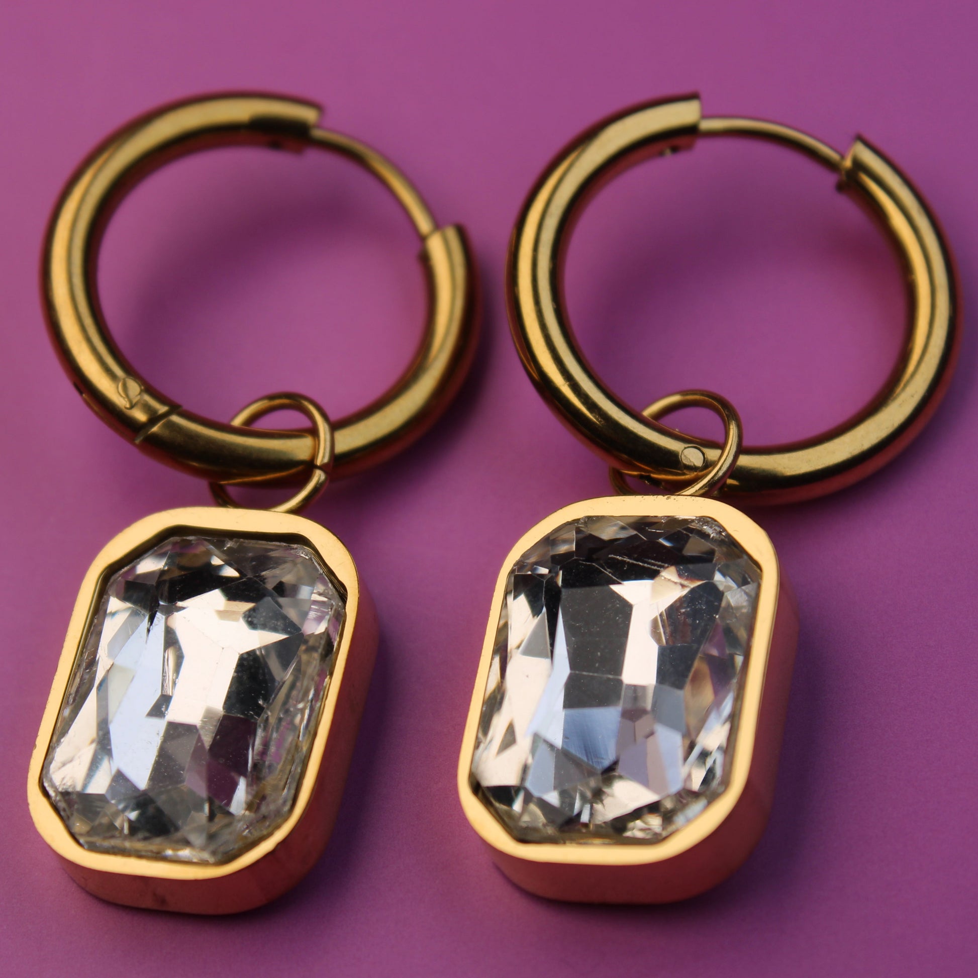 Gold hoop earrings with crystal-like stones on a purple background