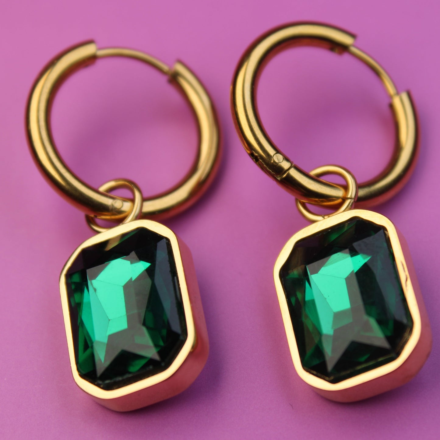 Gold hoop earrings with green gemstones on a pink background