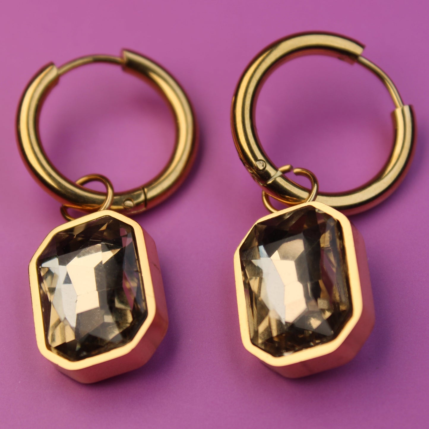 Gold hoop earrings with smoky quartz-like stones on a purple background