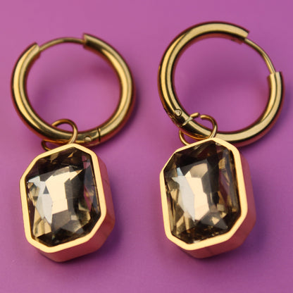 Gold hoop earrings with smoky quartz-like stones on a purple background