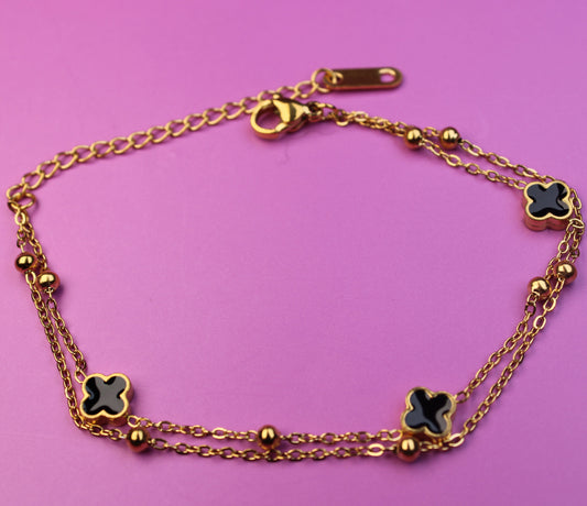 Gold bracelet with clover-shaped charms on a pink background
