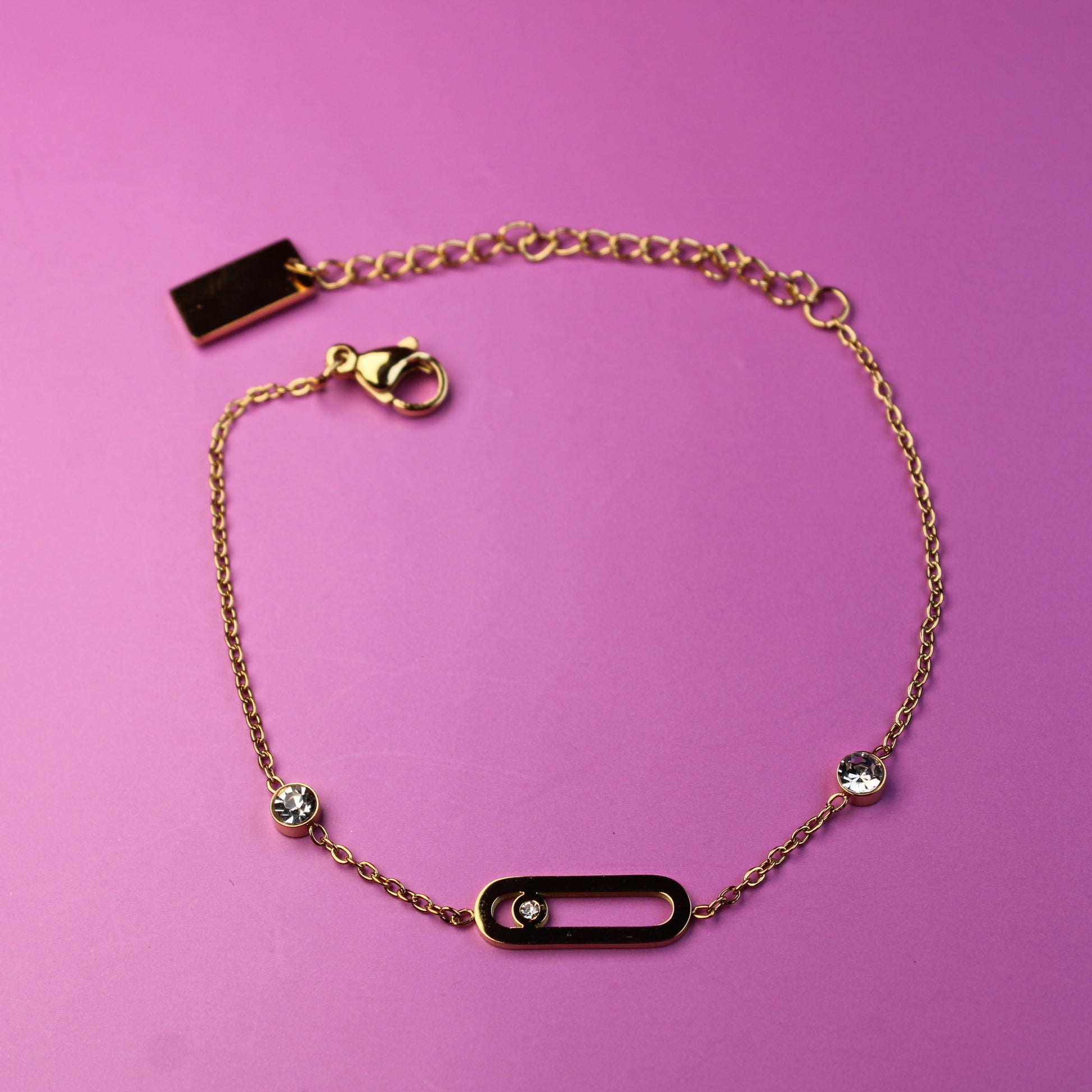 Gold bracelet with black rectangular charms on a pink background