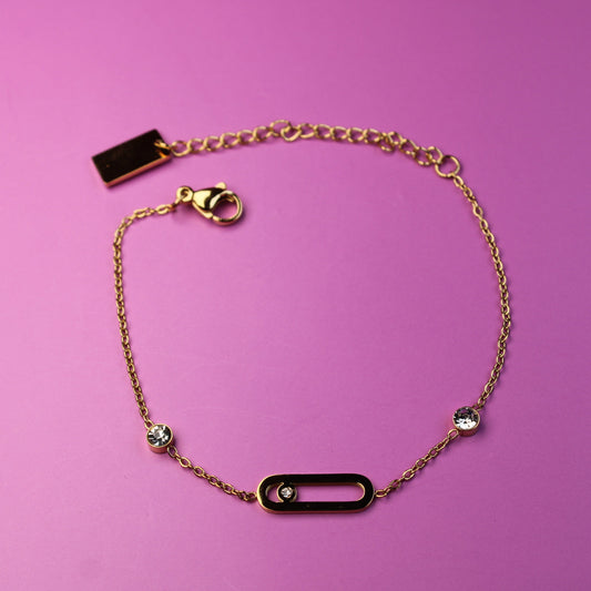 Gold bracelet with black rectangular charms on a pink background
