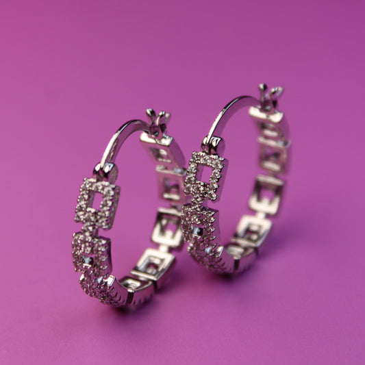 Pair of silver hoop earrings with gemstones on a pink background