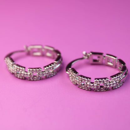 Pair of silver hoop earrings with pink gemstones on a pink background