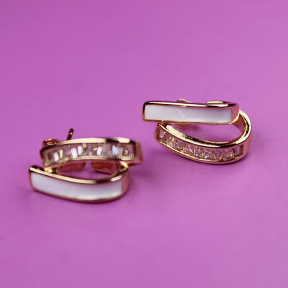 Pair of gold hoop earrings with white stones on a pink background