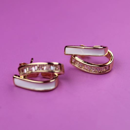 Pair of gold hoop earrings with white stones on a pink background