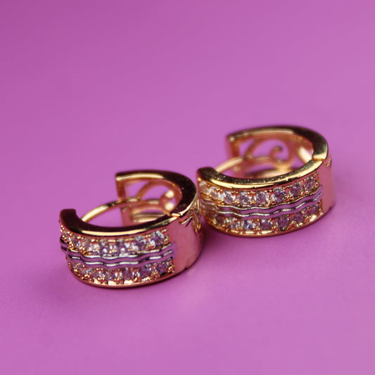 Gold hoop earrings with gemstones on a pink background