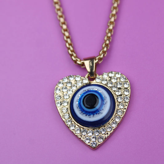 Heart-shaped pendant with a blue eye design on a gold chain against a pink background