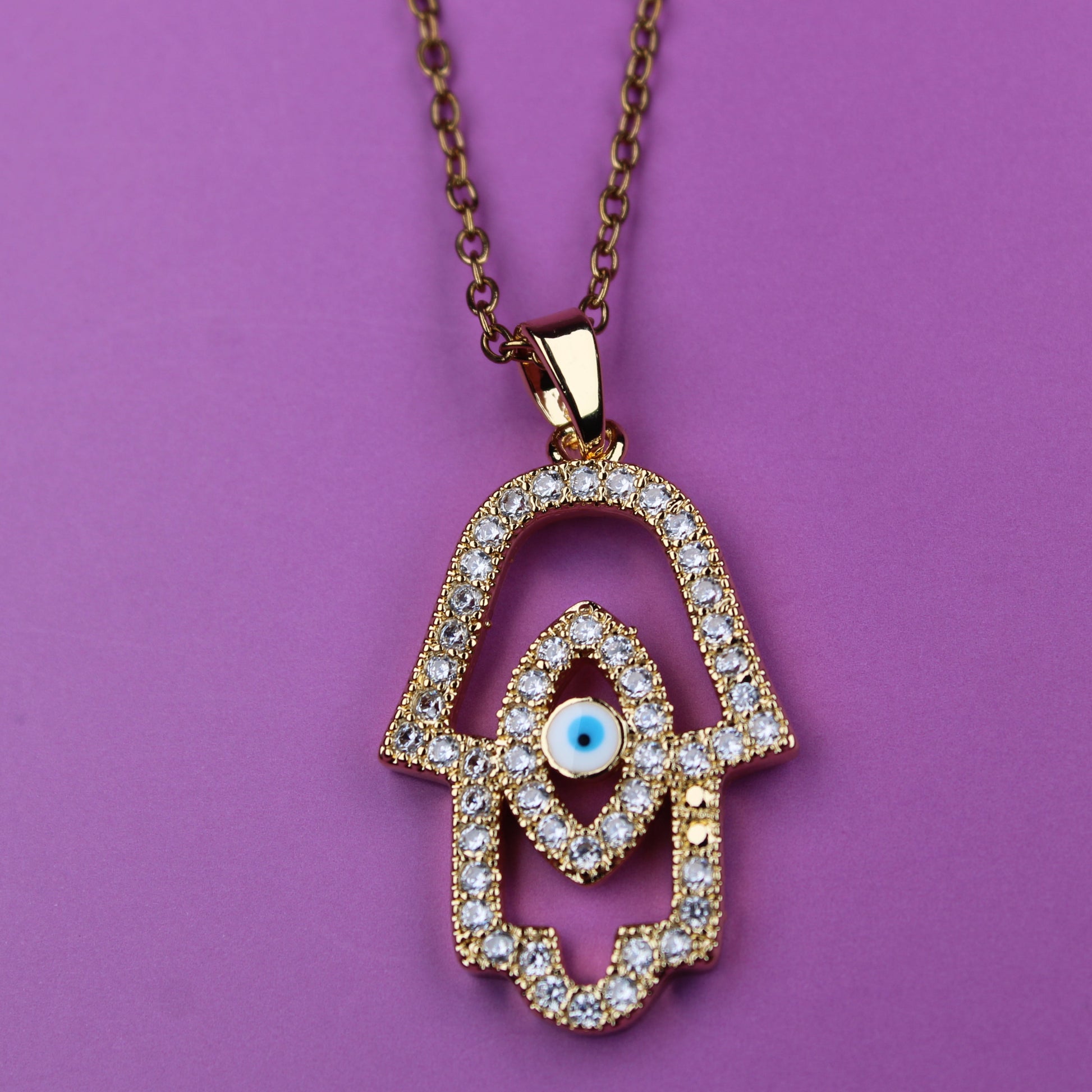 Gold Hamsa hand necklace with diamonds on a purple background