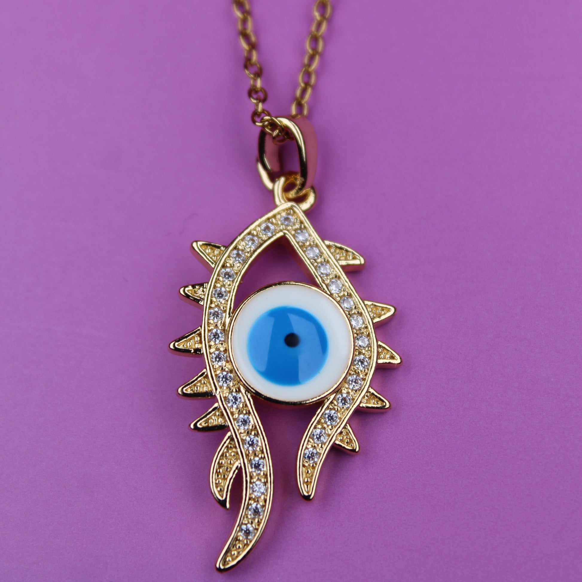 Gold necklace with an eye-shaped pendant on a purple background
