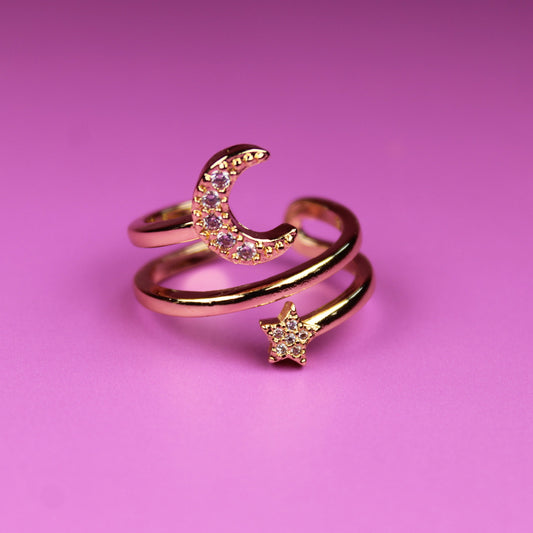Gold ring with moon and star design on a pink background