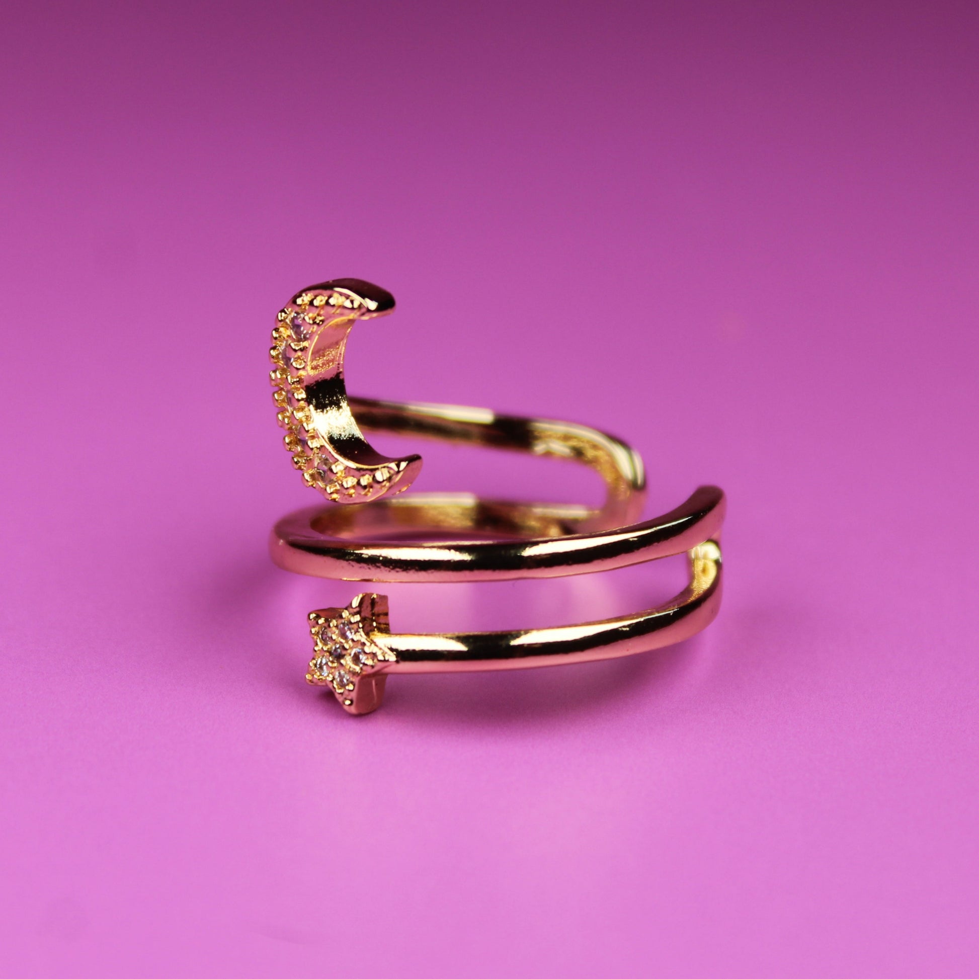 Gold ring with moon and star designs on a pink background