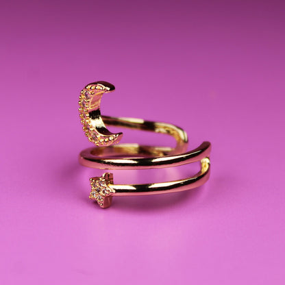 Gold ring with moon and star designs on a pink background