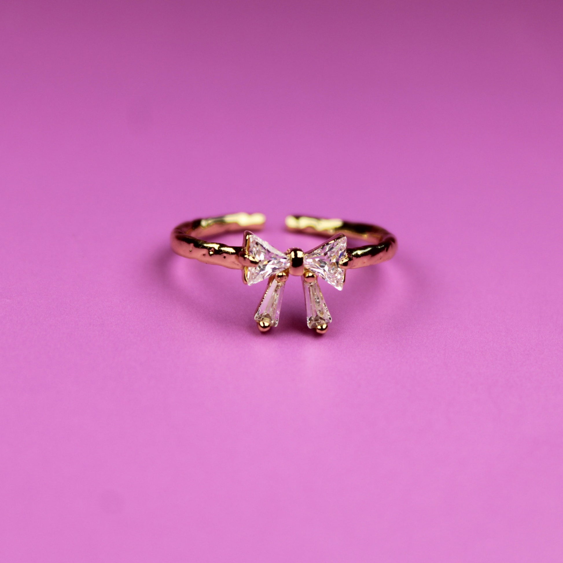 Gold bow-shaped ring on a pink background