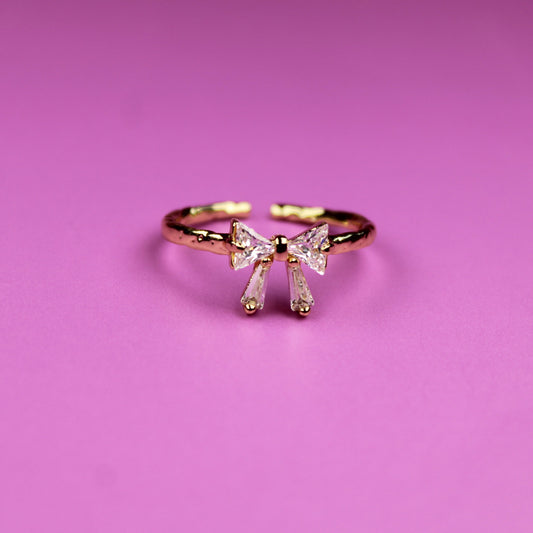 Gold bow-shaped ring on a pink background