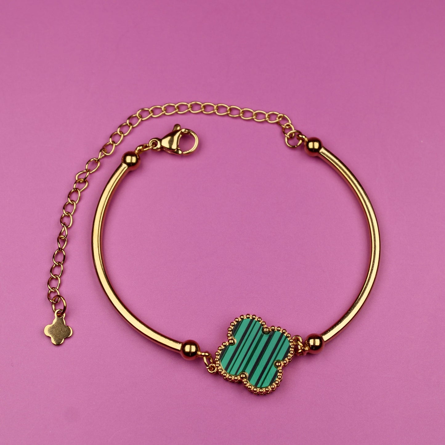 Gold bracelet with a green stone on a pink background