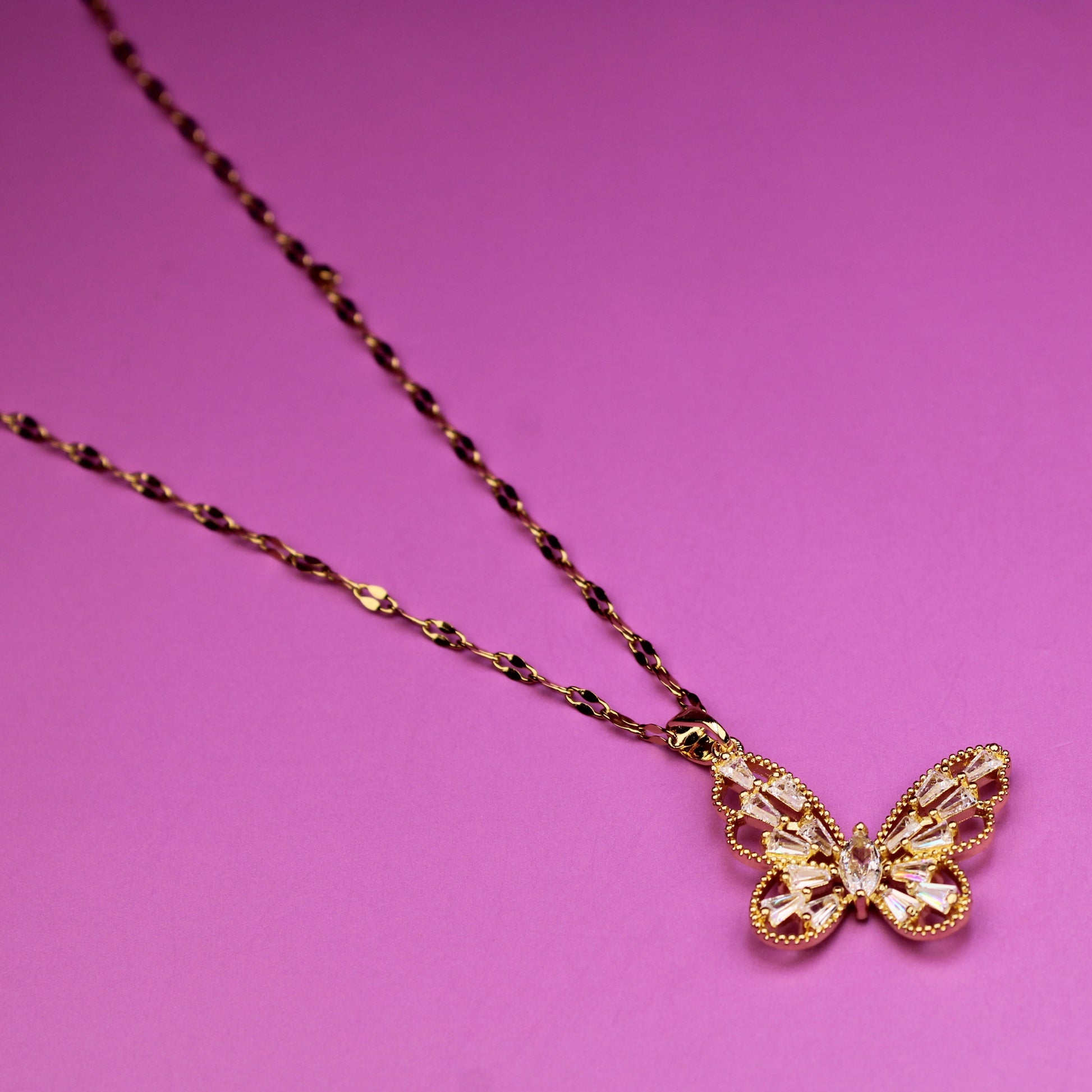 Gold butterfly pendant necklace on a pink background