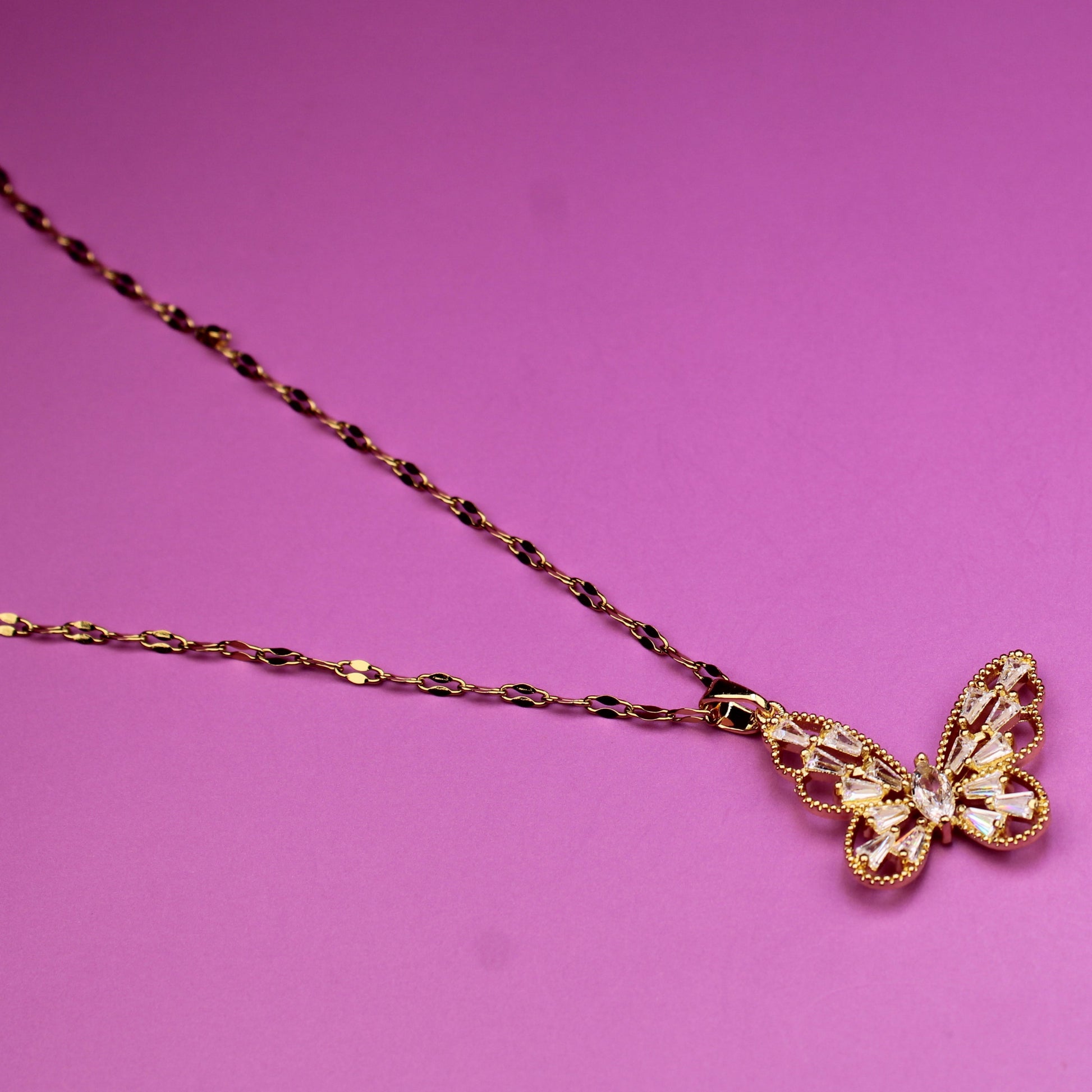 Gold butterfly pendant necklace on a pink background