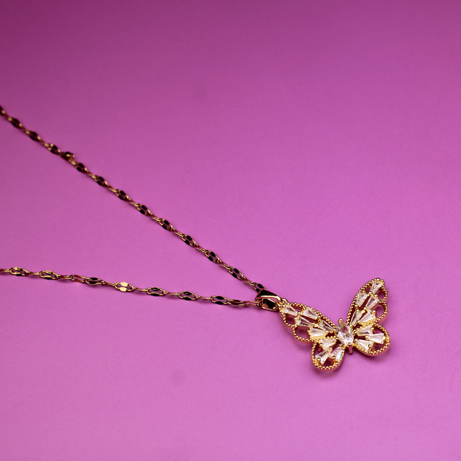Gold butterfly necklace on a pink background