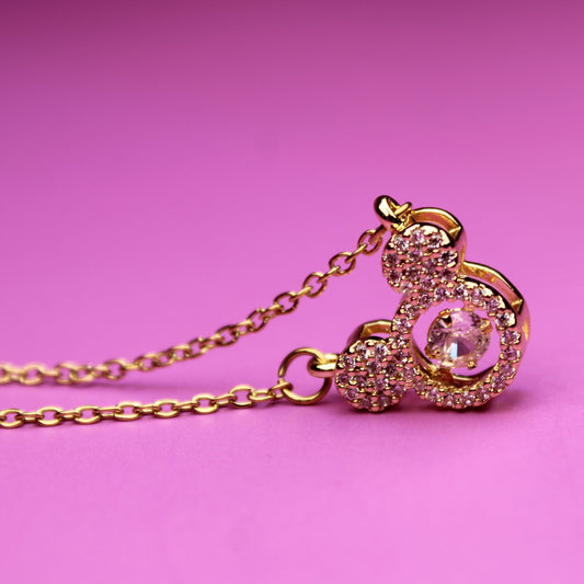 Gold necklace with a pink heart pendant on a pink background