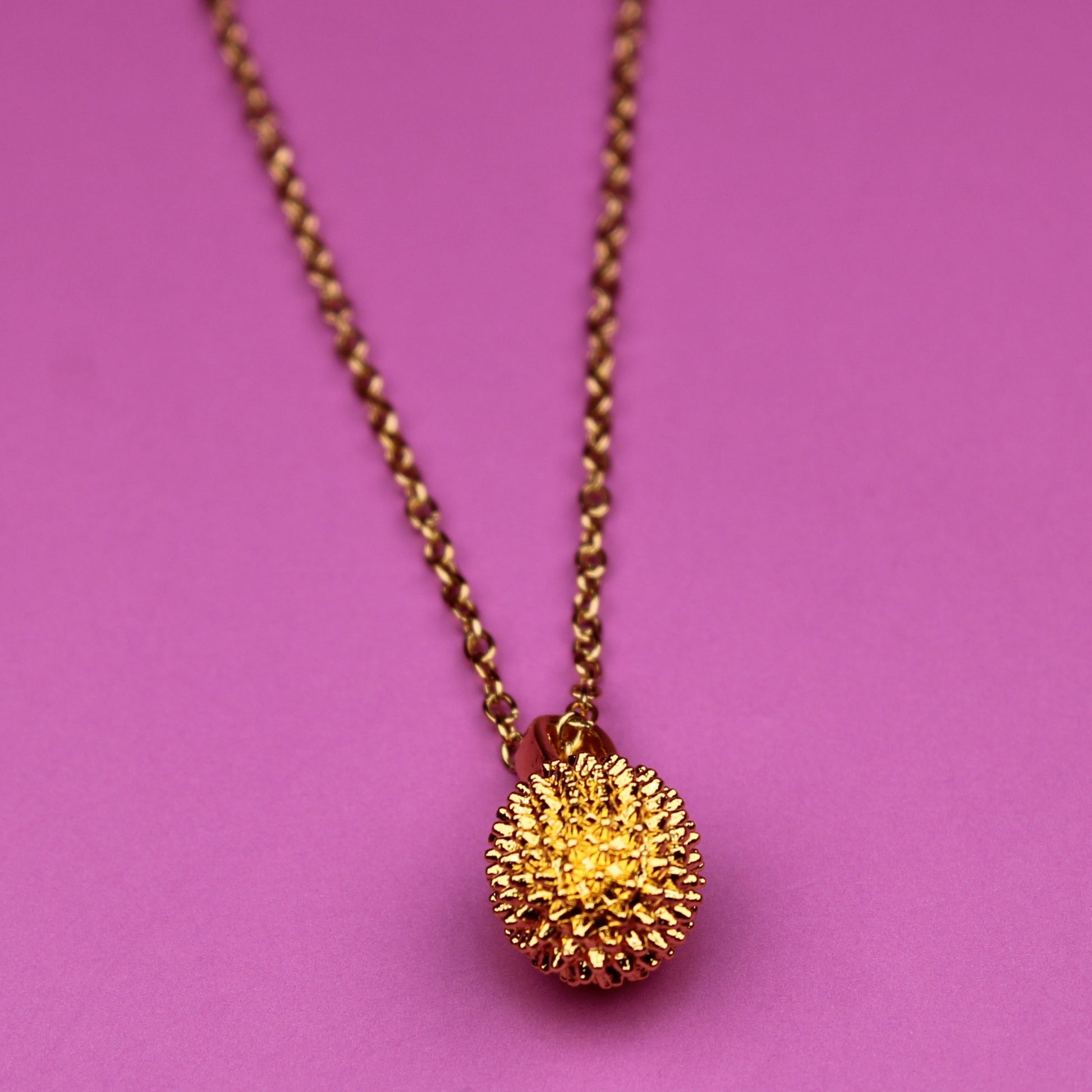 Gold necklace with a spherical pendant on a pink background