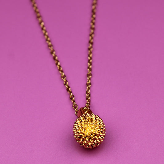 Gold necklace with a spherical pendant on a pink background