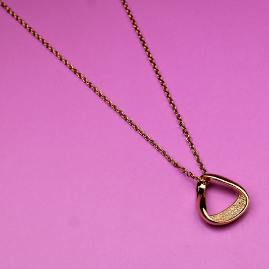 Gold necklace with a heart-shaped pendant on a pink background