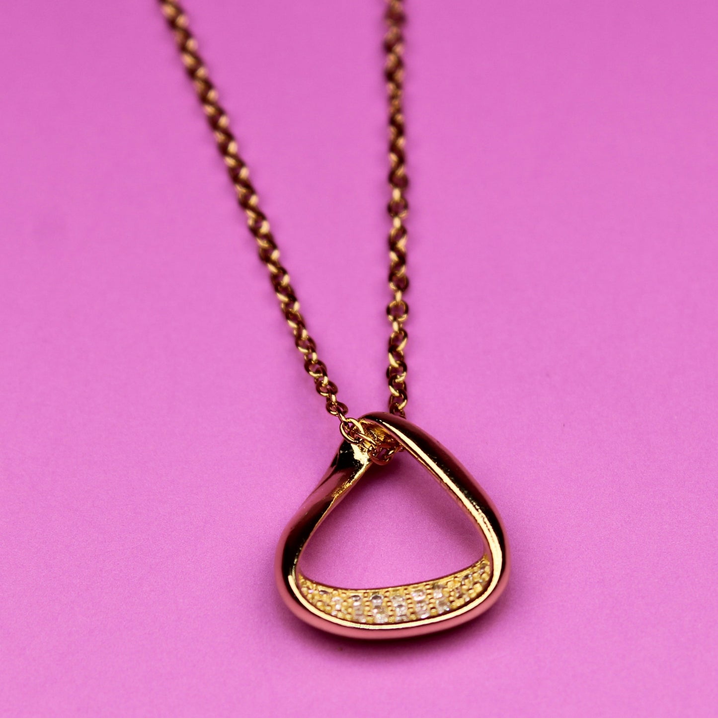 Gold necklace with a unique pendant on a pink background