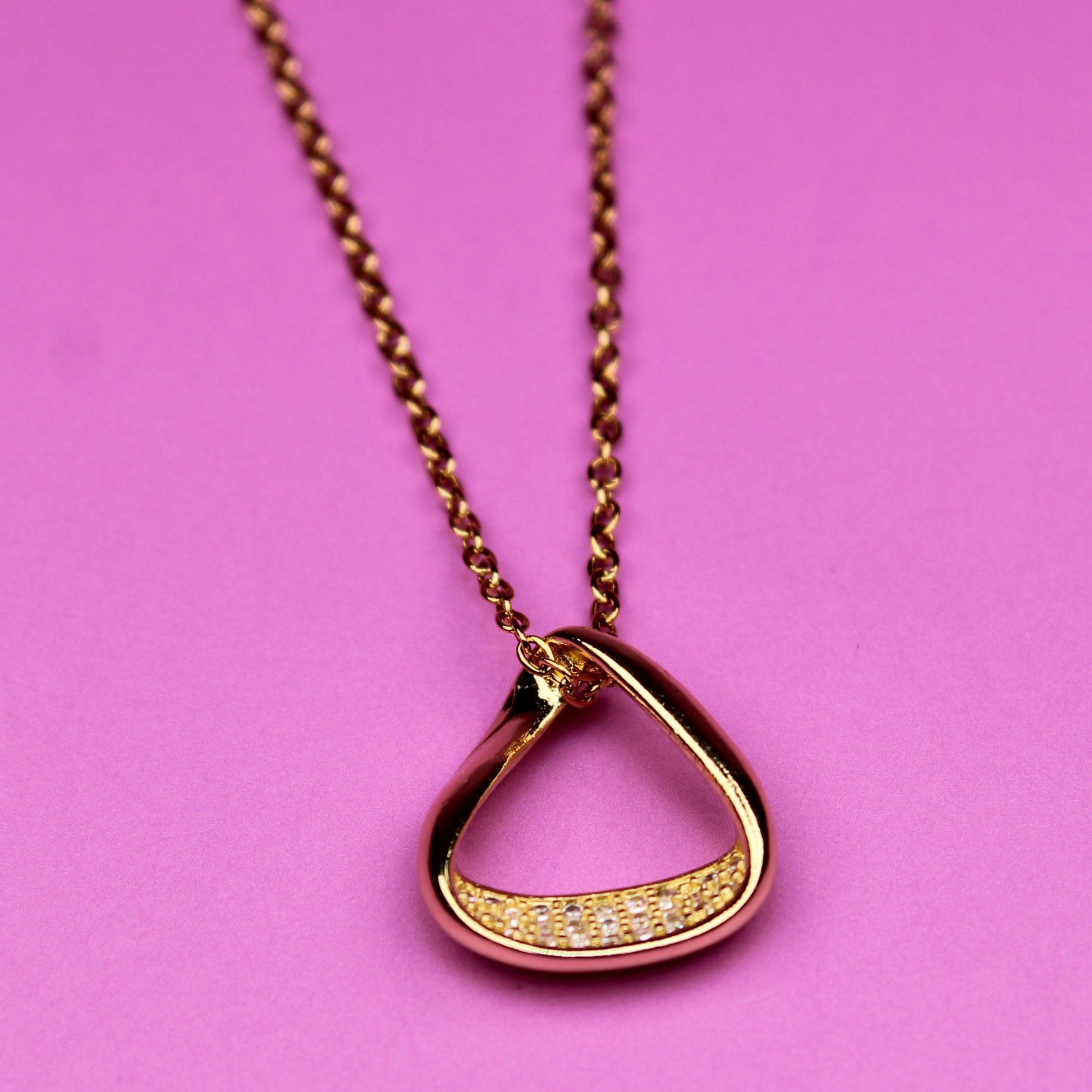 Gold necklace with a unique pendant on a pink background