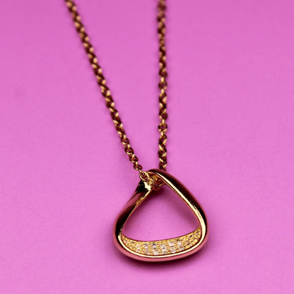 Gold necklace with a unique pendant on a pink background