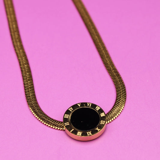 Gold necklace with a black pendant on a pink background