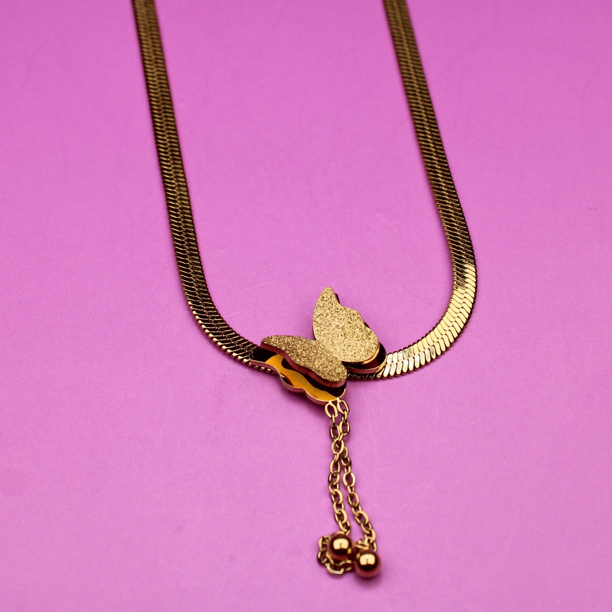 Gold necklace with a butterfly pendant on a pink background