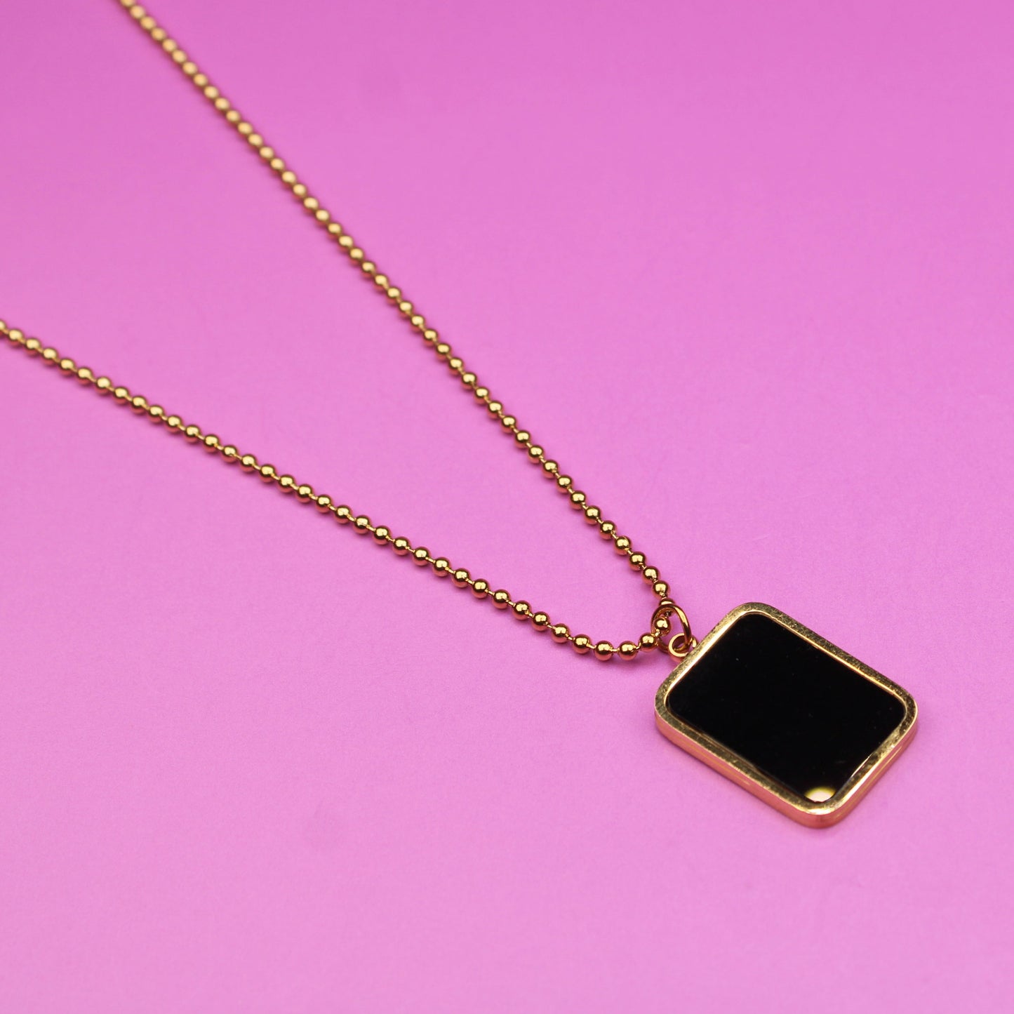 Gold necklace with a black pendant on a pink background