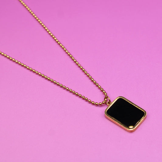 Gold necklace with a black pendant on a pink background