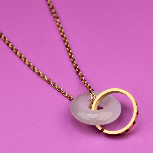 Necklace with a gold ring and white pendant on a pink background