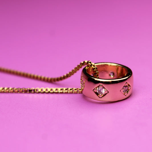 Rose gold ring with diamond accents on a chain against a pink background