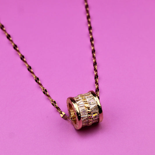 Gold necklace with a cylindrical pendant on a pink background