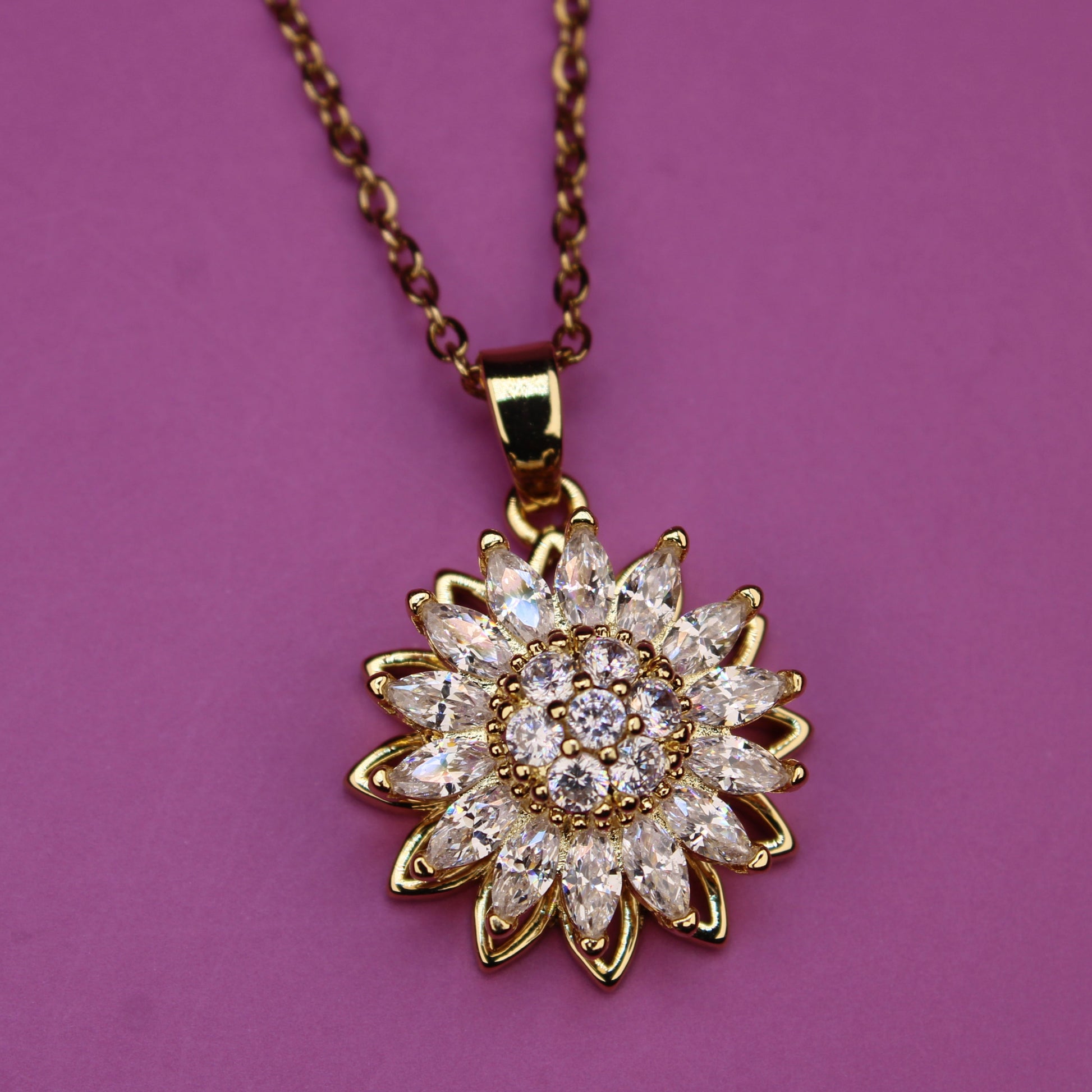 Gold necklace with a sunflower-shaped pendant on a purple background