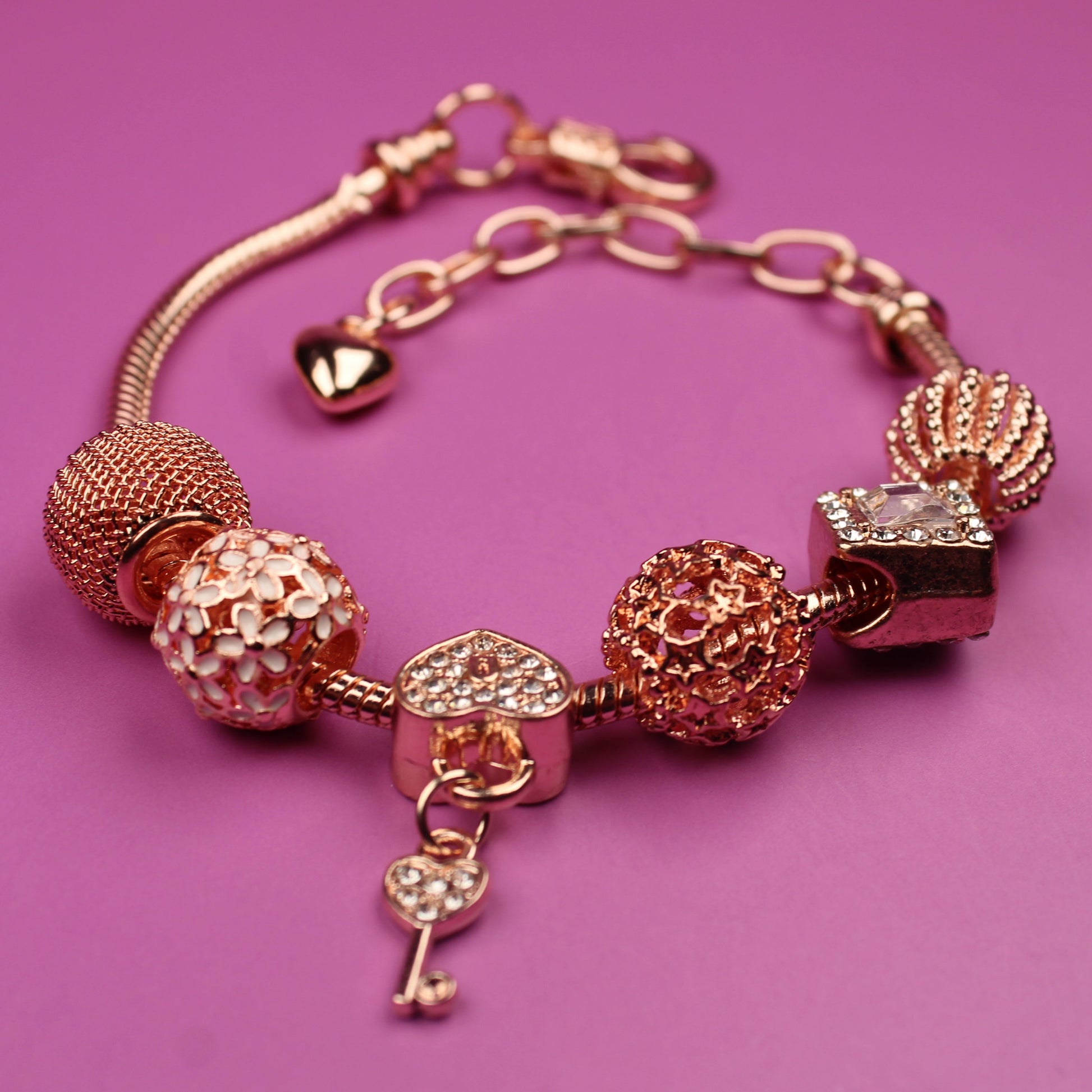 Rose gold bracelet with various charms on a pink background