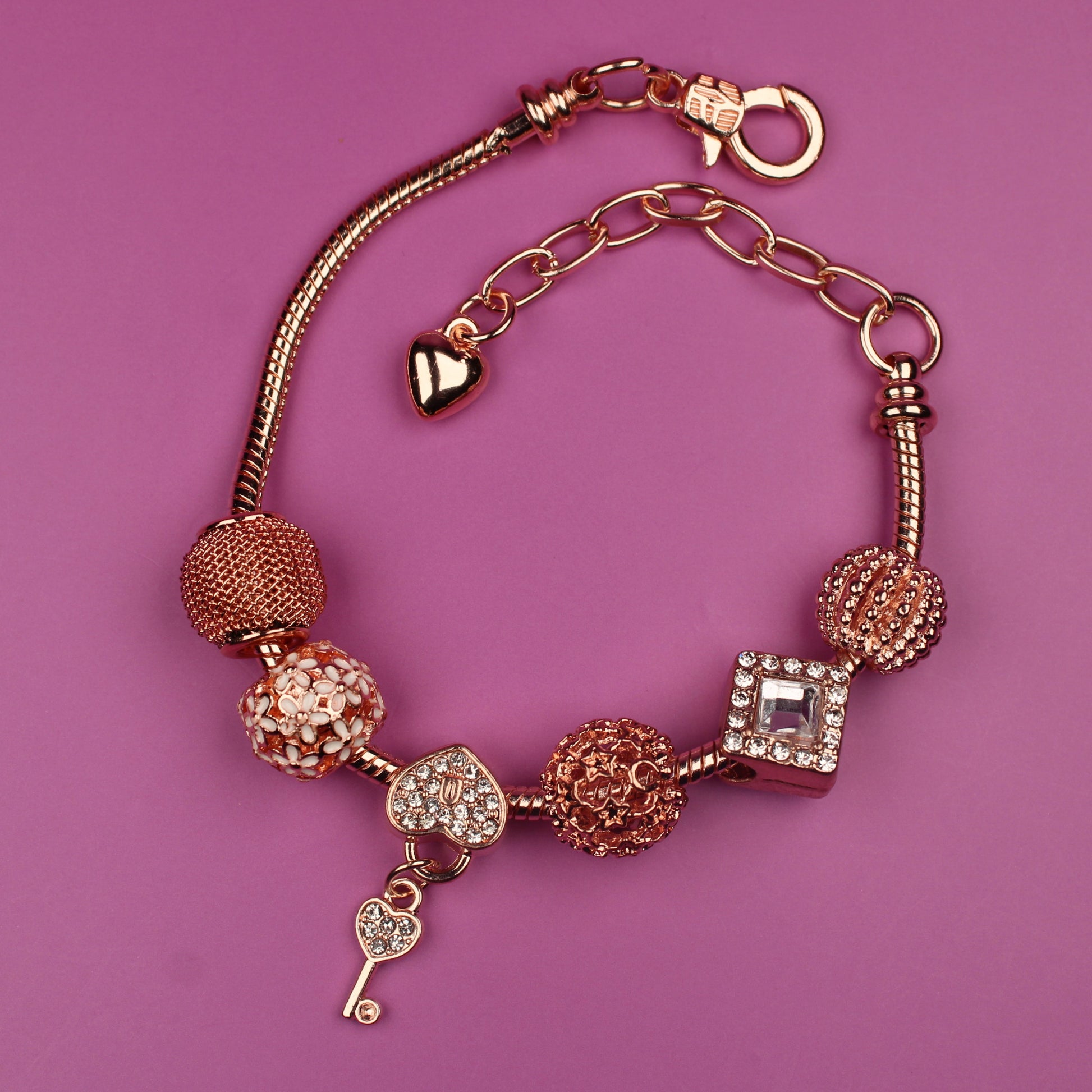 Gold bracelet with various charms on a pink background