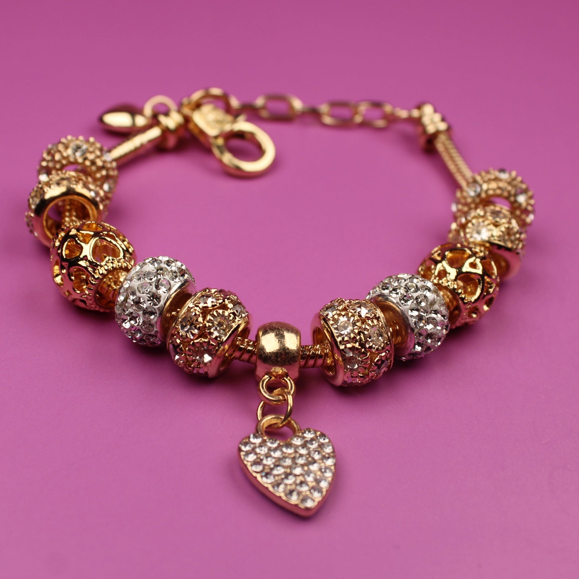 Gold bracelet with heart charm on a pink background